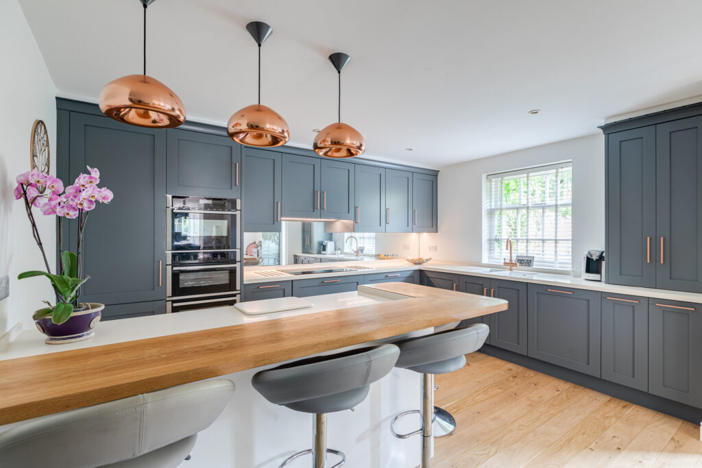 Dark grey lay-on shaker kitchen with copper pendant lights, an oak breakfast bar and a mirror splashback